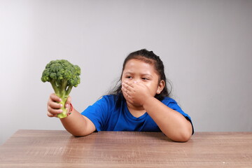 Adorable asian little girl refusing to eat broccoli, disgusted with broccoli