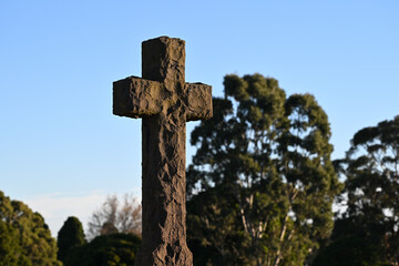 Stone cross, or crucifix, featuring a rough and textured surface, with trees in the background