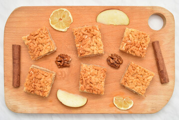 Pieces of homemade apple pie, walnut kernels, cinnamon sticks and slices of lemon and apple on the wooden cutting board. Top view. 