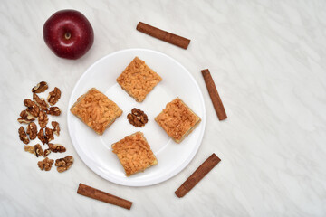 Pieces of homemade apple pie, walnuts, cinnamon sticks and apple on the light gray marble table texture. Copy space. Top view.