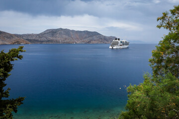 Scenic sea coast landscape at Symi island, Greece. 
A big white cruise ship on water. 