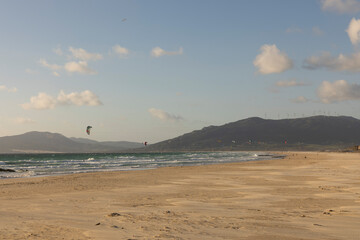 Landscape of Tarifa beach with kite surfers surfing waves in ocean on a bright day.