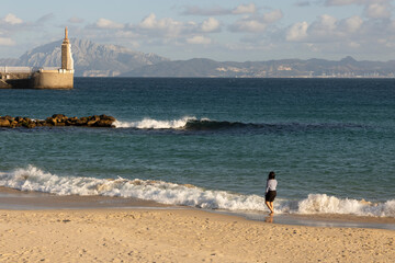 Tourists on the beach at statue of Jesus in Tarifa harbor on a bright sunny day