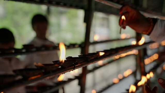 Devotees light oil lamps at Buddhist temple in Kandy, Sri Lanka. Hands hold flames in spiritual ritual. Worshipers perform traditional puja, kindle lights for blessings.