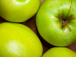 Green apples with a fresh sheen, some with brown spots, on a neutral background.