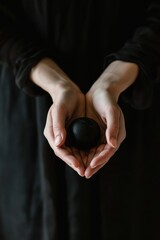 Close-up of hands gently holding a smooth black egg-shaped stone against a dark background