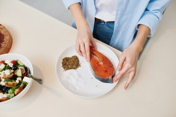 Woman preparing healthy meal with salmon and salad on a plate at home