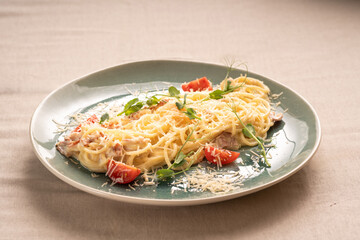 Pasta carbonara served with bacon in a creamy sauce garnished with tomatoes on a plate. Italian traditional menu