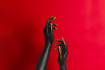Black and gold colors painted woman's hands on her skin with red background. High Fashion art...
