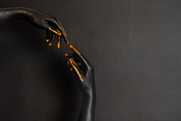 Woman's hands with black and gold paint on her skin on dark background. High Fashion art concept