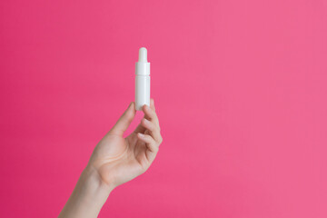 Serum white glass bottle or essential oil with pipette on pink background. Luxury cosmetic products...