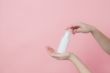 White unbranded cream bottle with pump in hand on pink background. Concept of beauty. Product...