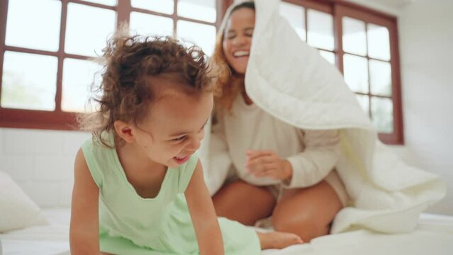 Happy little girl playing peekapoo to hide in blanket with mother together in bedroom at home. Mom and little daughter using spare time together at warmth house. Family relationship concept.