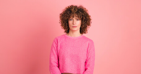 Standing charming young woman with curly hair in pink background