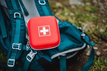 A first aid kit sits atop a blue backpack by a motor vehicle