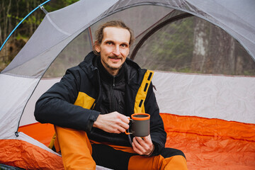 Man enjoys leisure time in tent, sipping coffee with a smile on his face