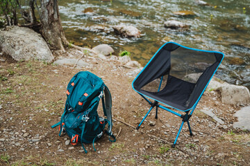 A chair and backpack rest by river in woodland landscape