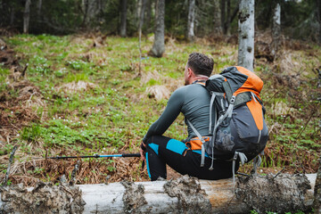 A man sits on a log in the forest with a backpack