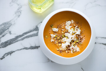 Bowl of sweet potato soup topped with feta cheese and pistachios, horizontal shot on a white marble background with space, high angle view - Powered by Adobe