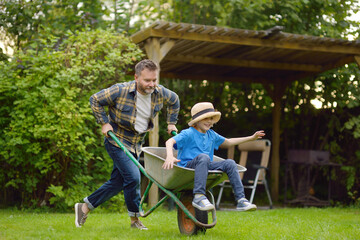Wheelbarrow pushing by dad in domestic garden on warm sunny day. Active outdoors games for family...