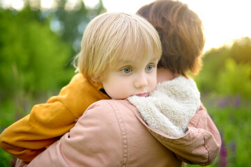 A woman holds a little child in her arms while walking through a blooming field. Cold weather in...