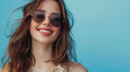 Fototapeta premium A stylish young woman in sunglasses smiling against blue background.