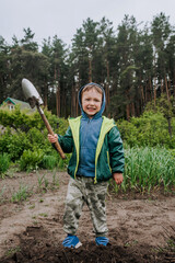 Little boy, happy child helps to dig soil with a shovel in the garden outdoors. Photography, portrait, agricultural concept, childhood.