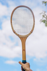 A young girl plays, holding a sports wooden retro tennis racket in her hands against the sky outdoors. Photography, sport concept.
