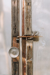 Close-up photo of an old closed door with latch of an oilcloth and wood greenhouse.