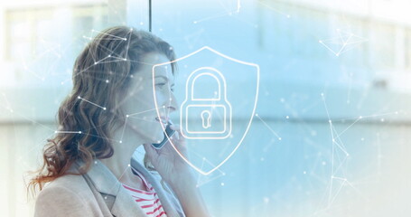 Image of padlock in shield, connected icons over caucasian woman talking on smartphone