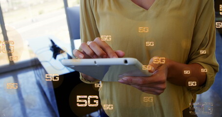 Image of multiple 5g text over midsection of biracial woman standing and using digital tablet