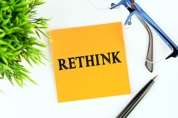 Rethink Business Concept text on a yellow sticker on a light background next to glasses, a pen and...