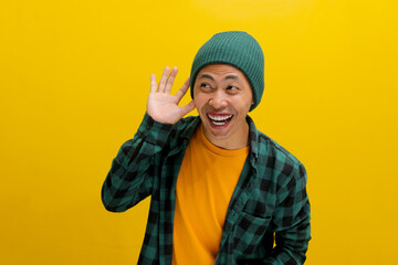 Young Asian man, dressed in a beanie hat and casual shirt, laughs while listening intently, hand cupped over his ear, possibly catching wind of rumor or gossip while standing against yellow background