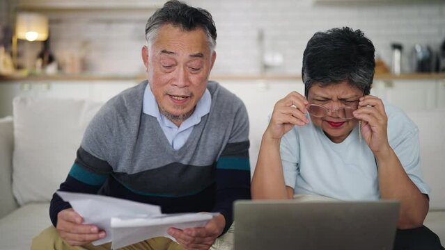 Asian Senior couple at home, feeling frustrated as they review their household finances on laptop