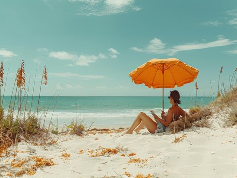 beach umbrella stuck in the sand, under which a person sits in sunglasses and reads book.