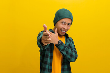 Confident young Asian man, points at the camera with a finger gun gesture, displaying confidence,...