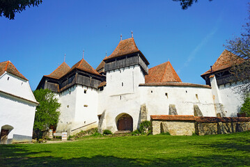 Fototapeta na wymiar Exterior view of a fortified church in the village of Viscri, Romania. Medieval landmark of Transylvania: fortress with defensive walls, numerous towers and a church in a Romanian village.