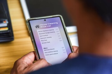 Man reading the current price list for house cleaning service on the mobile phone. Selective focus.