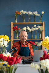 Portrait of an elderly male florist, small business owner of a florist shop sitting in his store...