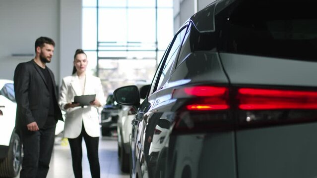 Bearded male buyer selects a car in a car dealership with the help of a car salesman. Concept of buying and selling a car, car rental and car service.