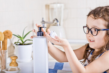 Little kid child washing hands with soap dispenser in a kitchen. Mock-up white container.