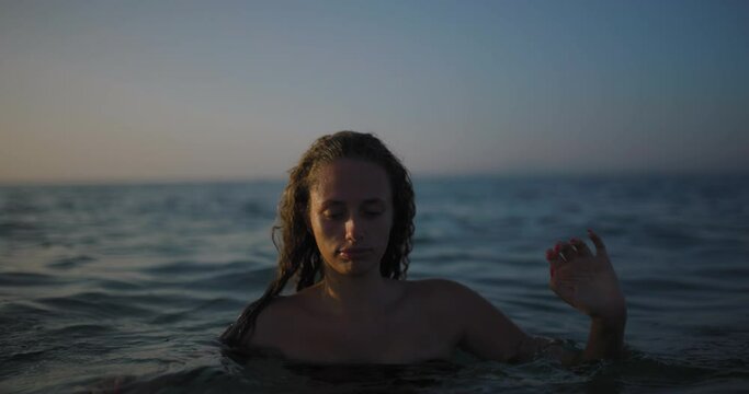 Young woman emerging from the sea at dusk with serene expression