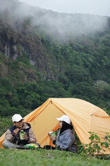 Fototapeta premium A couple is camping near a yellow tent in a beautiful mountain area with fog