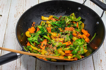 Vegan stir fry consisting of broccoli, carrot, peppers cooked in steel wok