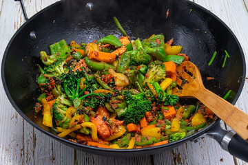 Vegan stir fry consisting of broccoli, carrot, peppers cooked in steel wok