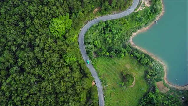 Aerial top down 4k view of white car driving on country road in forest in the evening at twilight. Cinematic drone shot flying over gravel road in pine tree forest