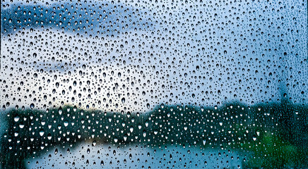 Raindrops clinging to window, blurred nature backdrop, texture of wet glass, close-up view of water droplets, moody atmosphere during rainy weather