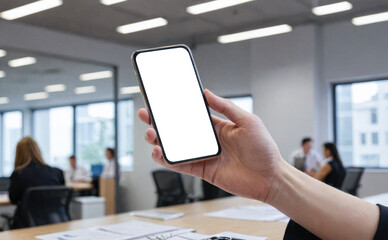 Person in office environment hold cellphone with empty white screen, ideal for app developers or advertisers, mobile and writing materials on desk, urban view through window