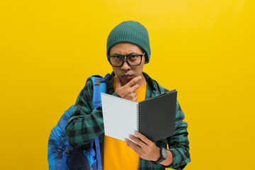 Pensive Asian student, wearing eyeglasses, a beanie hat, and casual clothes, carrying backpack,...