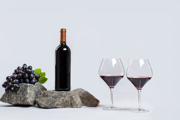 Bottle on stones and two glasses with red wine on a white background